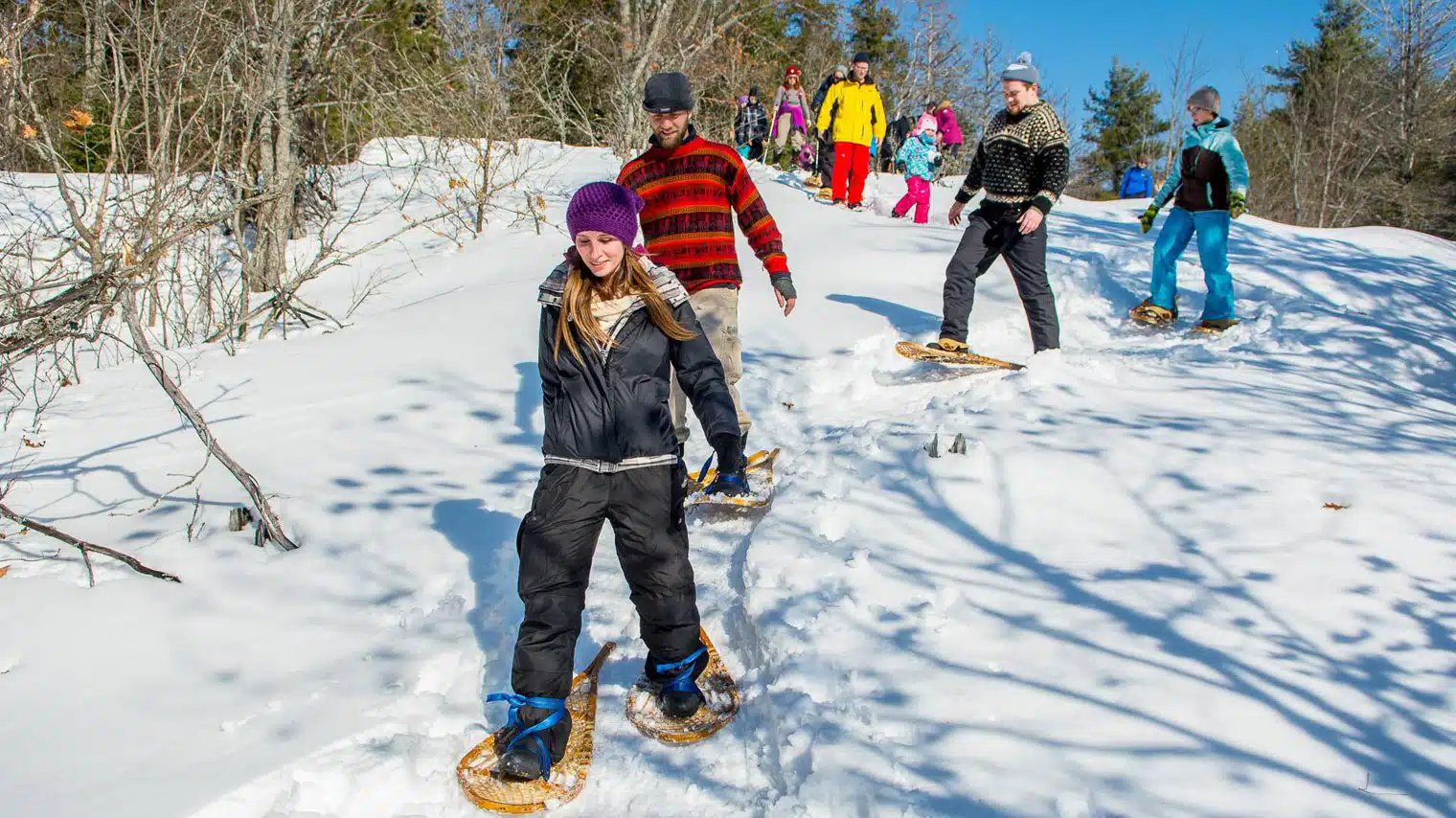 A group snowshoeing down a sunny, snowy hill